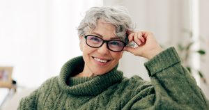 A mature individual with short gray curly hair, black-rimmed glasses, and a green turtleneck sweater, in a bright casual indoor setting, illustrating credit protection through fraud alerts and security freezes.