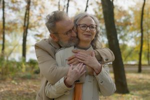A senior couple shares a loving embrace in an autumn park, with the man hugging his wife from behind amid colorful fall foliage, symbolizing gratitude for family, love, and life's simple joys that inspire mindful financial habits.